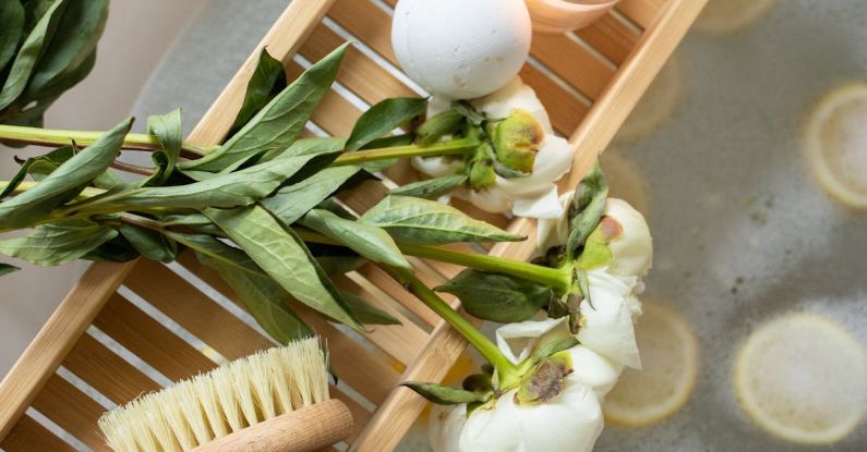 Sanitizers - Top view of wooden tray with bath bomb and burning candle placed near salt and flowers on tub with lemon slices on water