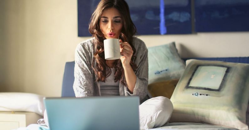 Streaming Services - Woman in Grey Jacket Sits on Bed Uses Grey Laptop