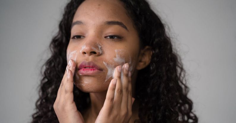 Water Purifiers - African American female with long dark curly hair washing cheeks with facial foam on gray background