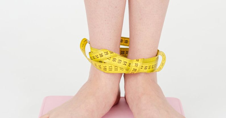 Monitor Stands - High angle of crop anonymous female with centimeter on legs checking weight on scales on white background